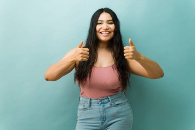 Stüdyoda gülümseyen Latin bir kadın iki başparmak hareketiyle onay ve pozitifliğini dile getiriyor.