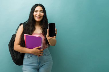 Okul kitaplarını tutan, sırt çantası takan ve cep telefonunu kopyalayan genç bir kadın. Eğitim ve teknoloji kavramı