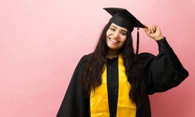 Gülümseyen bayan öğrenci, kolej başarısını kutlamak için sarı atkıyla kep ve cübbe giyiyor.
