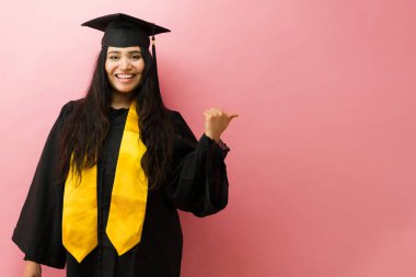 Mezuniyet elbisesi ve şapkası giyen mutlu İspanyol kadın başarıyı kutluyor ve parmağıyla işaret ediyor.