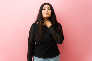 Latin kadın boğaz ağrısı ya da hastalıktan muzdarip. Pembe arka planda rahatsızlığını dile getiriyor.