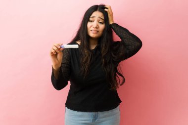 Elinde hamilelik testi tutan genç bir kadın pembe stüdyo geçmişine karşı tedirgin ve endişeli hissediyor.