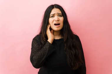 Şiddetli diş ağrısı çeken bir kadın, pembe stüdyo arka planında yanağına dokunuyor, dişçiye ihtiyacı var.