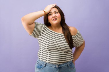 Şişman bir kadın, kafası karışık ve endişeli hissediyor, elleriyle alnına dokunuyor, stres yaşıyor ya da unutkanlık yaşıyor.