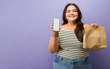 Çevrimiçi yemek servisi portresi yapan, boş bir akıllı telefon ekranı ve kahverengi bir kese kağıdı gösteren kıvrımlı bir kadın.