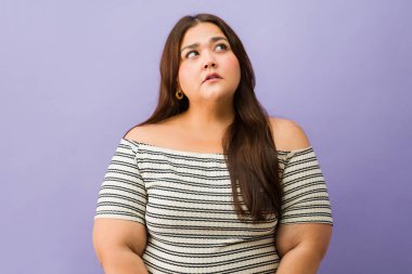 Düşünceli, iri yarı bir kadın yukarı bakıyor, düşünüyor, bir fikri var ya da sağlam bir mor arka planı merak ediyor.