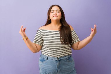 Gözleri kapalı duran bir kadın, stüdyo arka planında stres atmak için meditasyonla iç huzurunu ve dengesini buluyor.