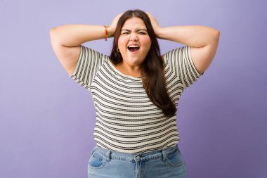 Artı boyunda bir kadın çığlık atıyor, yoğun duygular gösteriyor, stres, hayal kırıklığı ya da öfke yüzünden kulakları ellerle kapatıyor.