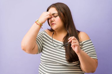 Latin kadın yoğun baş ağrısı ya da migren hissediyor, gözlük çıkarıyor ve kronik ağrı ve göz yorgunluğu nedeniyle burnunu sıkıyor.