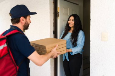 Kurye, ev girişinde mutlu bir bayan müşteriye bir yığın karton pizza getiriyor, hızlı servisi vurguluyor.
