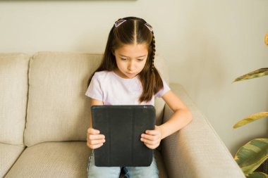 Kanepede yemek, ders çalışmak ve eğlenmek için tablet kullanan odaklanmış bir kız.