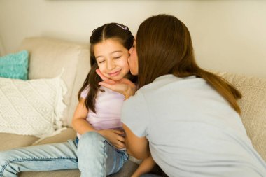 Sevgi dolu anne, neşeli kızına yanağından yumuşak bir öpücük verir. Evdeki kanepede yan yana uzanır, sevgi ve yakınlık gösterir.