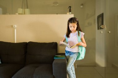 Sırt çantalı bir kız kitap okuyor, okul ödevlerine konsantre oluyor ve akademik başarıya çalışıyor.