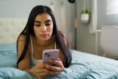 Kadın yatakta yüzüstü yatıyor, cep telefonunu karıştırıyor, diğerleriyle bağlantı kuruyor ve rahatlatıcı bir sabah geçiriyor.