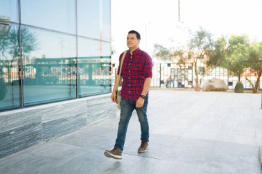 Yetişkin bir adam ekose gömlek ve kot pantolon giyerek şehir kaldırımında işe gidiyor.