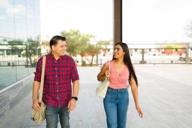 Gülümseyen genç bir çift birlikte yürürken sohbet ediyorlar. İspanyol erkek ve kadın şehir merkezinde gündelik bir gezinti yapıyorlar.