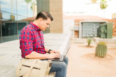 Adam dışarıda otururken bilgisayarına odaklanıyor, uzaktan çalışma, teknoloji bağlantısı ve modern iş-yaşam dengesi kavramlarını resmediyor.