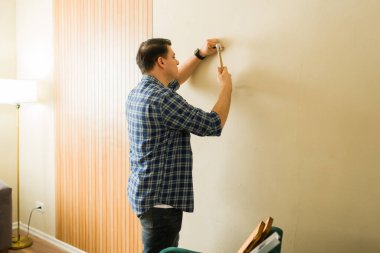 Adam duvara çivi çakıyor, ev yapımı proje üzerinde çalışıyor. Dekorasyon yapıyor, evinin içini geliştiriyor.