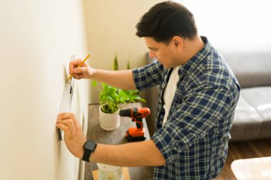 Evdeki diy projesine konsantre olan bir adam, bir ruh seviyesini ve kalemi kullanarak duvarı dikkatlice işaretliyor.