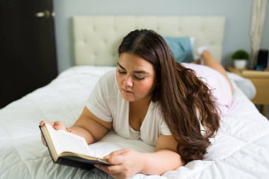 Ayrıca yatak odasında dinlenen, yatağa uzanmış kitap okuyan cüsseli bir kadın. Sakin bir sabah geçiriyor.