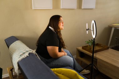 Genç, kıvrımlı kadın nüfuzlu kişi canlı yayın yapıyor, modern teknolojiyle sosyal medya takipçileri için çevrimiçi içerik yaratıyor.