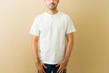 Bej arka planda beyaz tişörtlü bir adam, özel tasarım veya markalaşma için temiz bir model alanı sunuyor, stüdyo çekimi