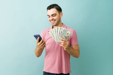 Gülümseyen adam finansal başarıyı buluyor, elinde akıllı bir telefonla para tutuyor, kazancı, karı ve mobil bankacılığı temsil ediyor.