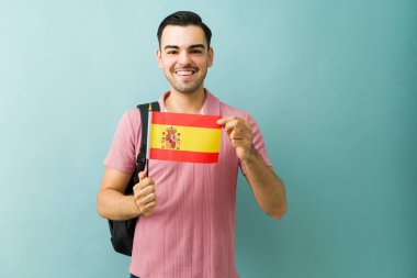 Öğrenci, sırt çantası taşıyan bir İspanyol bayrağını gururla tutuyor. Yurtdışında eğitim, seyahat ya da kültür deneyimlerini temsil etmek