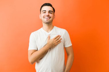 Samimi bir gülümseme ile ayakta duran, elini kalbine koyan minnettarlığını, minnettarlığını ve sadakatini ifade eden bir adam.