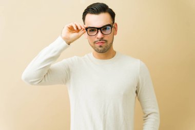 Şık gözlükler takan İspanyol bir adam ve açık renk bir süveter, sağlam bir arka plan karşısında kendine güvenini ve zekasını gösteriyor.