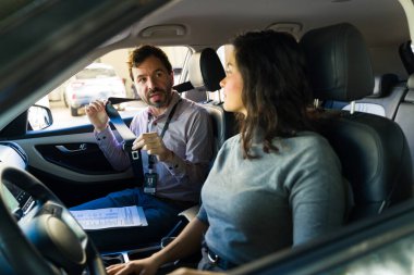 Sürücü eğitmeni, yetişkin bir kadına emniyet kemerini bir aracın içinde nasıl bağlayacağını gösteriyor.