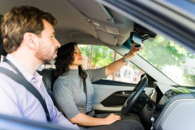 Yetişkin bir kadın araba kullanmayı öğreniyor, bir eğitmenle şoför koltuğunda otururken dikiz aynasını ayarlıyor.