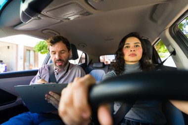 Yetişkin öğrenci sürücüsü, eğitmeni performansı izleyen ve not defterine not yazan bir araba kullanmayı öğreniyor