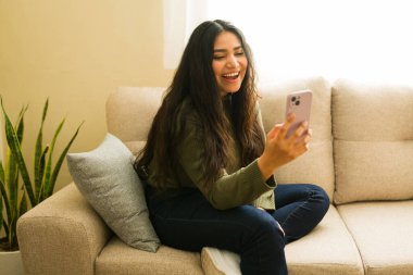 İspanyol bir kadın, evdeki bir kanepede dinlenirken cep telefonuyla video görüşmesinde biriyle mutlu bir şekilde konuşuyor.