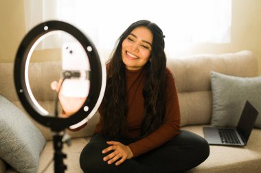 Gülümseyen kadın takipçiler için çevrimiçi video içeriği yaratıyor, evden yaşıyor, modern bir vlogger olarak çalışıyor.