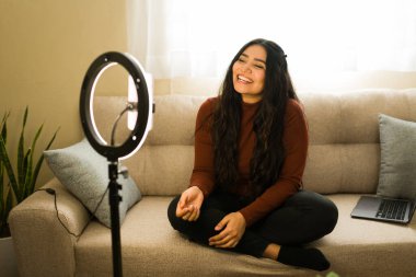 Çevrimiçi içerik oluşturan genç bir kadın, bloglama veya vloglama, bir kanepede oturan doğal ışık akışı