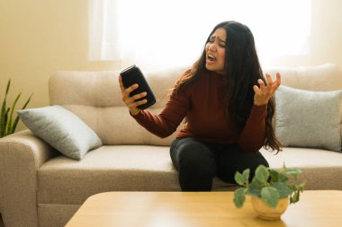 Genç bir kadın, yapay zeka cihazının çalışmamasından rahatsız ve kızgın hissediyor, evde teknolojik sorunlar ve sinir bozuklukları gösteriyor.