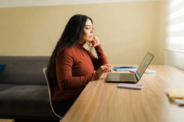 Bilgisayarına odaklanan bir kadın, çalışırken ya da internetten öğrenirken ahşap bir masada oturuyor.