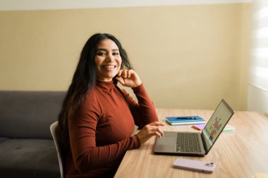 Gülümseyen ve internetten çalışan genç bir kadın. Uzak mesleki görevler ve verimlilik için dizüstü bilgisayar kullanan Latin Amerikalı iş kadını