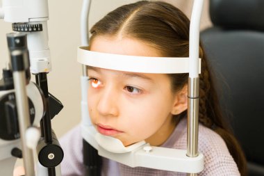 Çocuk göz muayenesi için göz doktoruna gidiyor. Kapsamlı bir görüş testi için kafasını yarık lambaya koyuyor.