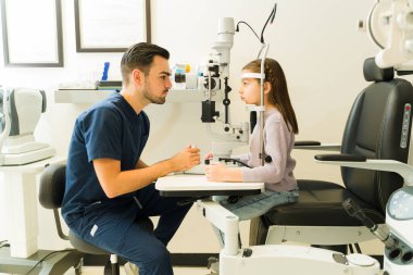 Erkek göz doktoru, yarık lamba mikroskobu kullanan bir çocuk üzerinde göz muayenesi yapıyor, görüşü kontrol ediyor ve potansiyel sorunları tespit ediyor.