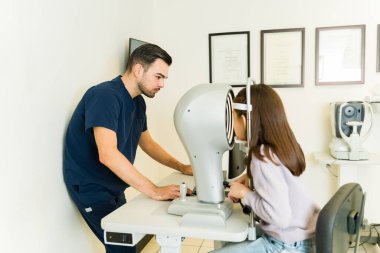 Optisyen hekim genç bir kadının görme yeteneğini göz hekimliği bürosunda ileri seviye teşhis araçlarıyla kontrol ediyor.