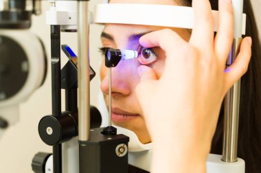 Göz doktoru muayenesinden geçen kadın hasta, glokom teşhisi için tonometre testi yapan doktor.