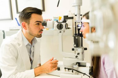 Erkek göz doktoru, yarık lamba mikroskobu kullanarak kadın bir hastaya göz muayenesi yapıyor.