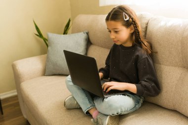 Küçük kız ev ödevi yapıyor. Evde dizüstü bilgisayarla oturuyor. İnternette eğitim arıyor.