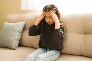 Kanepede oturan küçük bir kız, şiddetli bir baş ağrısı ya da migrenden muzdarip, evde acı ve sıkıntı yaşıyor.