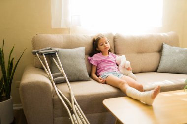 Koltukta dinlenen kırık bacaklı küçük bir kız. Koltuk değnekleriyle evinde yaralanmış.