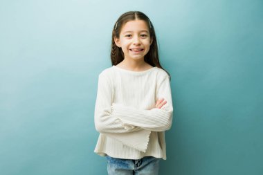 Kollarını kavuşturup kameraya gülümseyen mutlu küçük kız. Çocuk kendinden emin ve pozitif hissediyor