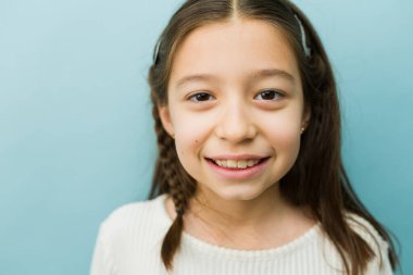 Mutlu bir ifadeyle poz veren küçük bir ilkokul çocuğu mavi bir arka plana gülümsüyor, sağlık hizmetlerini temsil ediyor.