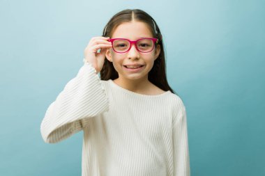 Genç kız gülümsüyor ve yeni pembe gözlüğünü ayarlıyor. Çocuk sağlığı, vizyon bakımı ve göz sağlığı kavramlarının temsilcisi